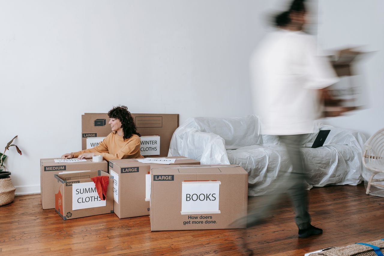 Un couple range des cartons étiquetés dans un salon minimaliste, en préparation du jour du déménagement.
